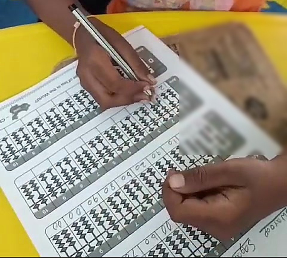 A child's hands working through an abacus practice worksheet during class