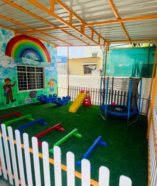 Empty outdoor play area at a preschool branch with artificial grass, balance beams, slide and trampoline